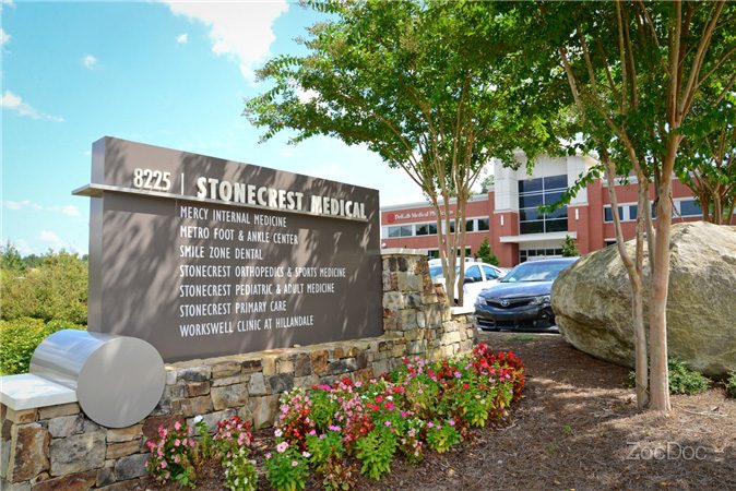 Stonecrest medical sign in front of a building with windows, surrounded by plants with flowers, a group of trees