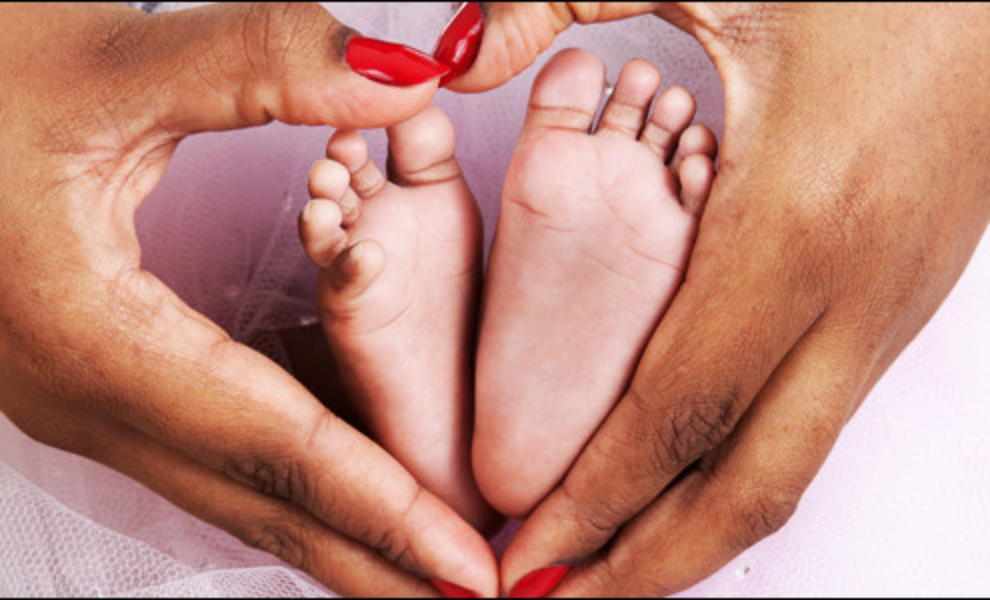 Woman holding a baby's feet in the shape of a heart, with her hands gently cradling them