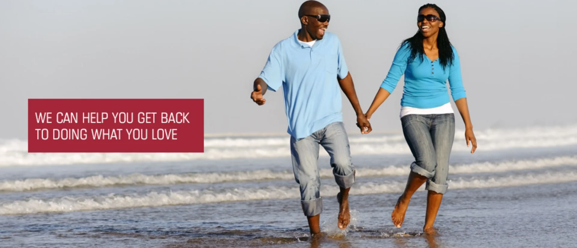 Man and woman walking hand in hand on the beach, both wearing sunglasses