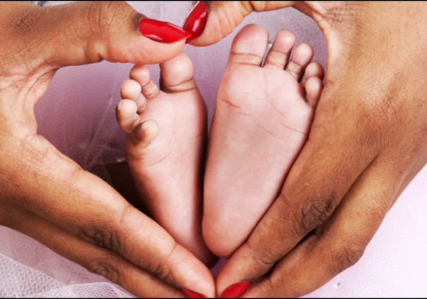 Woman holding a baby's feet in the shape of a heart, with her hands gently cradling them